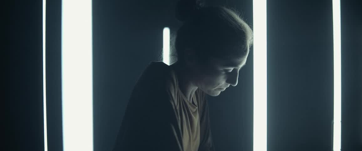 White woman dancing alone in a dark room with some wall lamps behind her