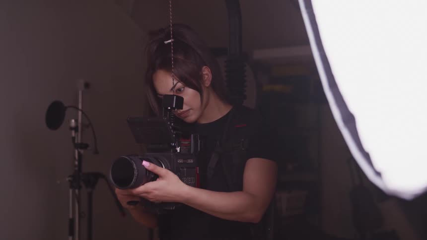 Photographer holding a camera next to a light in a dimly lit studio