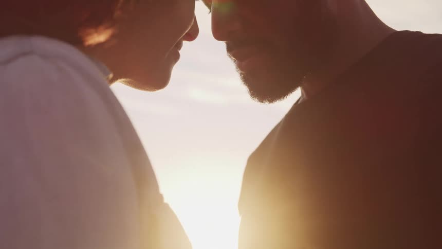 A man and woman lean their heads together and look at one another as the sun shines down on them