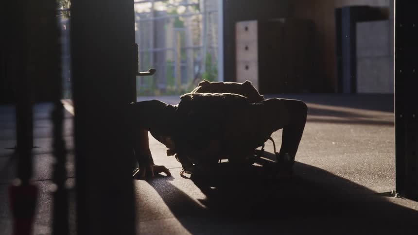 A man doing push ups with weights with a fence trees the sky and clouds in the background
