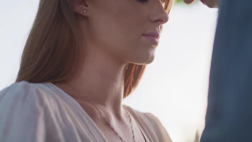 A woman wearing a white top stands outside with her eyes closed