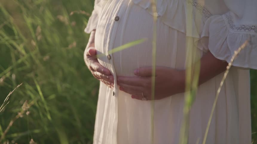A woman is standing in a field while touching her pregnant stomach