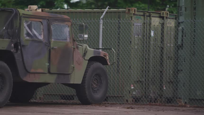 A cam painted jeep parked in front of a fence with trailer buildings