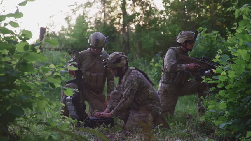 Three soldiers in camouflage uniforms and helmets stationed in the forest