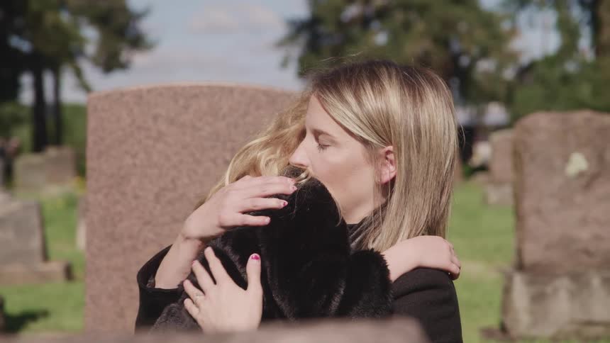 A woman is hugging a female child and rubbing her back in a cemetary