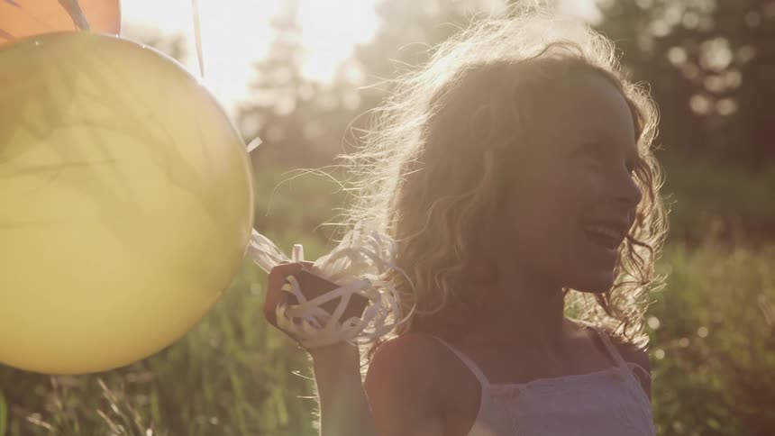White kid holding a yellow balloon and smiling in the middle of a grass field