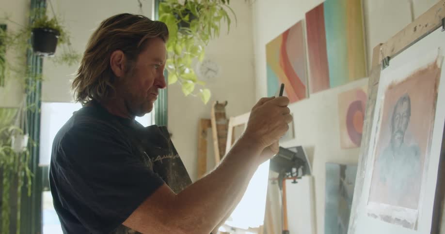 A middle aged man used a smartphone to take a photograph of a painting on an easel indoors during the day