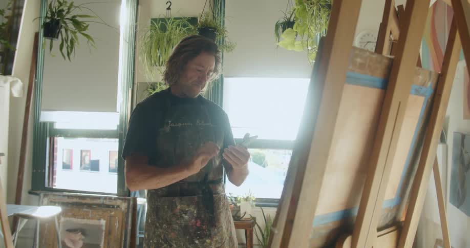 A man takes a picture of a painting on an easel with a smartphone in an art studio at daytime