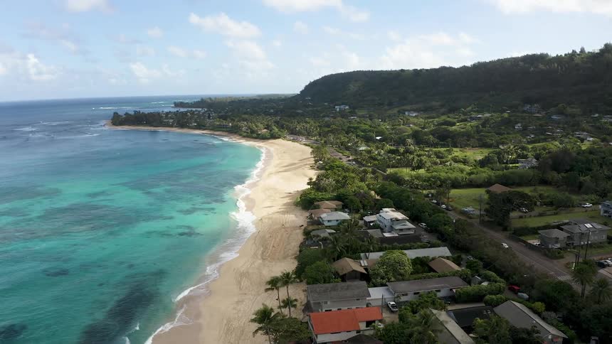 Aerial view of a coastal neighborhood with a beach and homes next to a road with driving cars at daytime