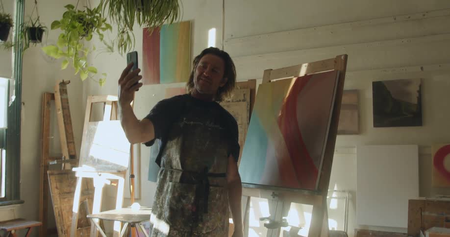 White man video calling someone on his smartphone and showing his painting