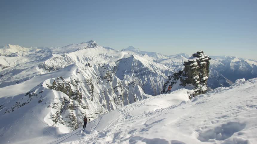 Two mountaineers standing atop the snow covered peak on a mountain range