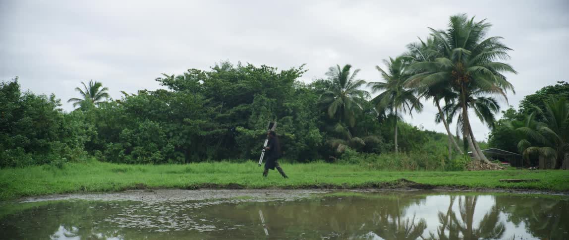 A man carries a large pole as he walks past a pond