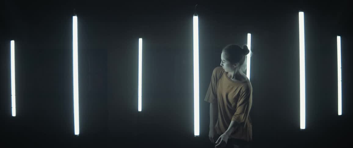 Young woman dancing around floating fluorescent lights inside a dark room