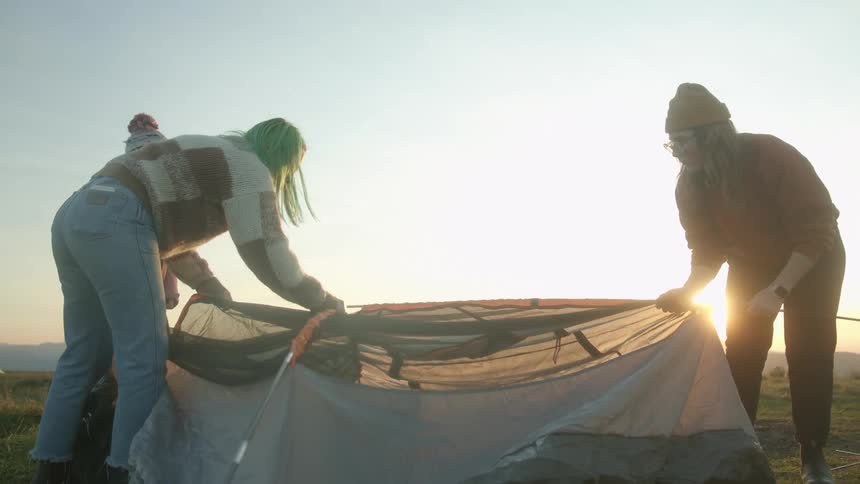 Three female friends erecting a tent camping on a mountain at sunset
