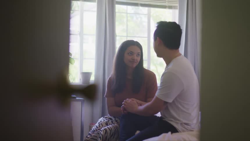 Young couple sitting in a bed holding hands looking at each other in a room at home