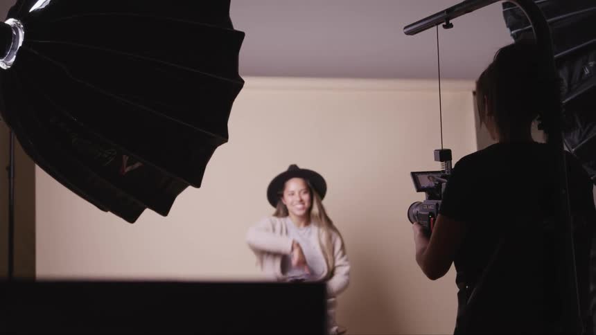 A girl is being photographed by another woman while she sits against a wall