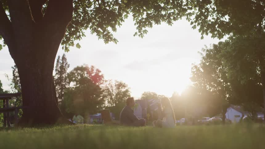 Young couple sitting over the green grass in a park talking to each other at sunset