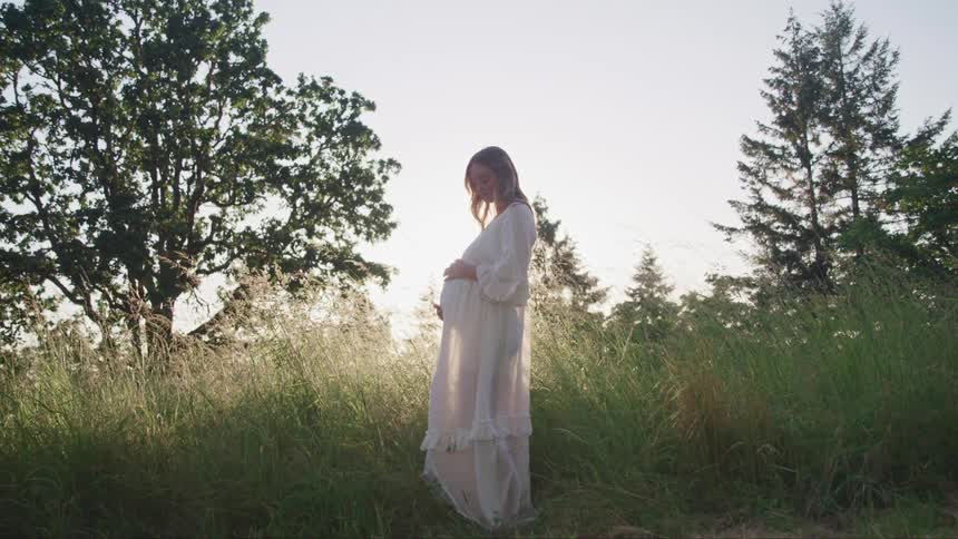 A pregnant woman standing in front of a field
