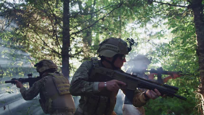 Three men with helmets and rifles in the forest with trees in the background