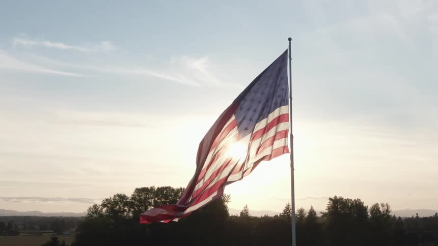 American flag flowing in the wind on a flag pole in front of a flare of sunlight at daytime