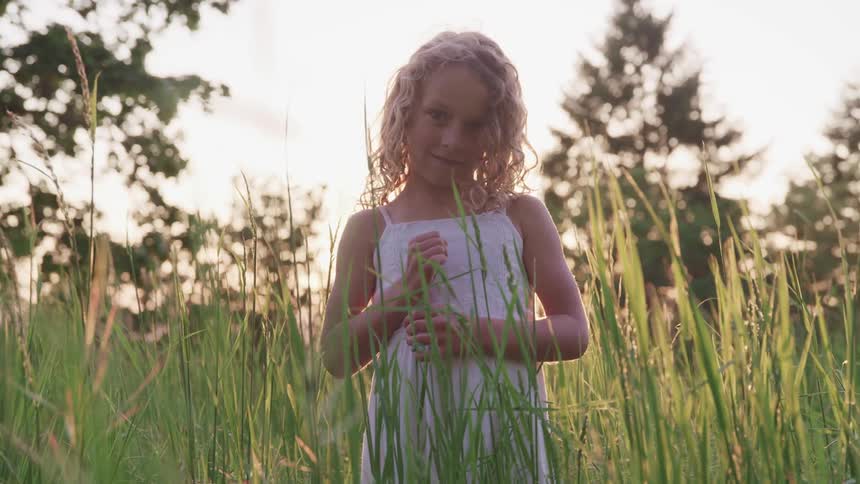 A young girl smiles as she stands in a field of tall grass