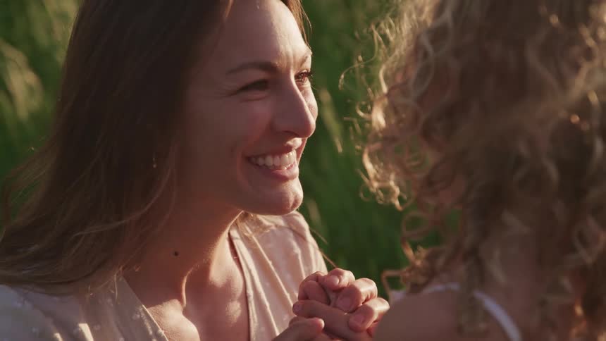 A woman smiles as she kneels down and holds her daughters hand