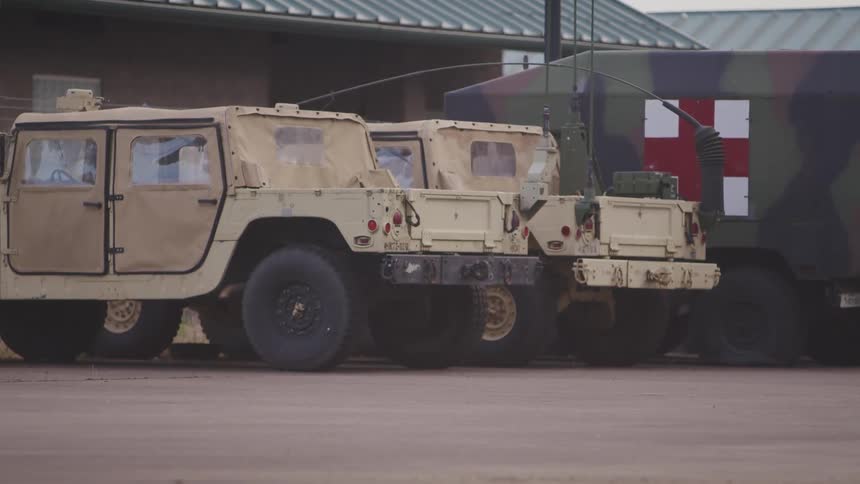 A pair of beige military hummers parked near a red cross camouflage truck