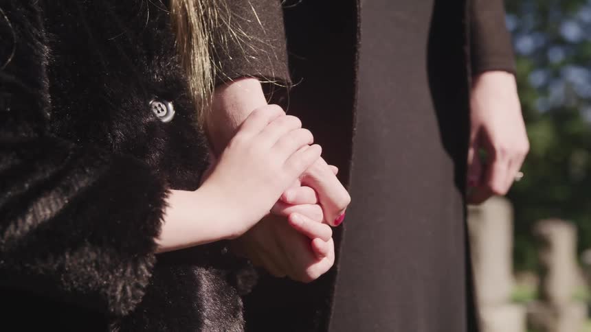 Two people holding hands at a graveyard