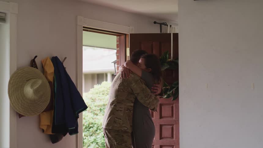 Military man and his wife hugging and looking each other in the eye close to the door