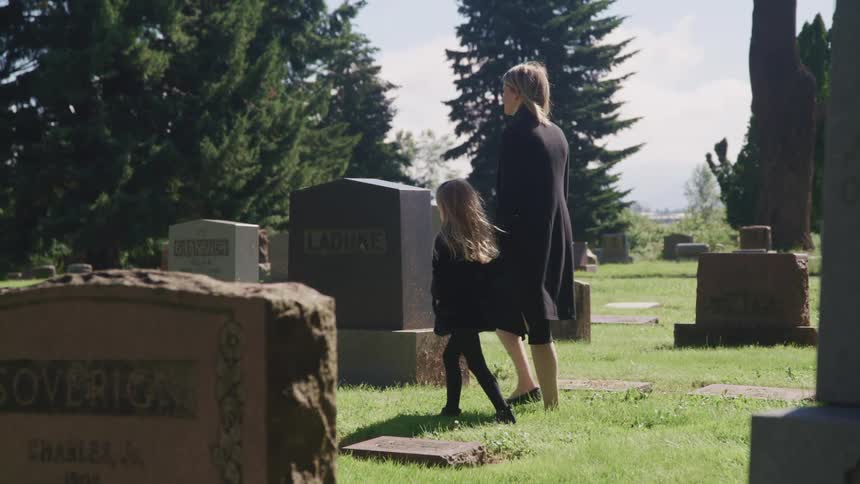 Mother holding her daughters hand walking in a cemetery at daytime