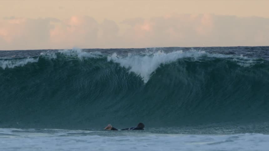 Surfer riding a surfboard in the ocean dives under a big wave at sunset
