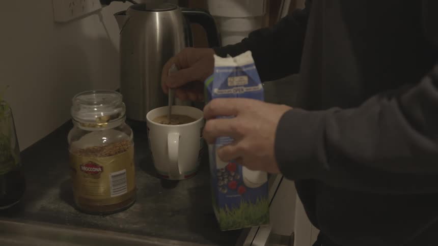 A man adds milk to his coffee and stirs with a spoon