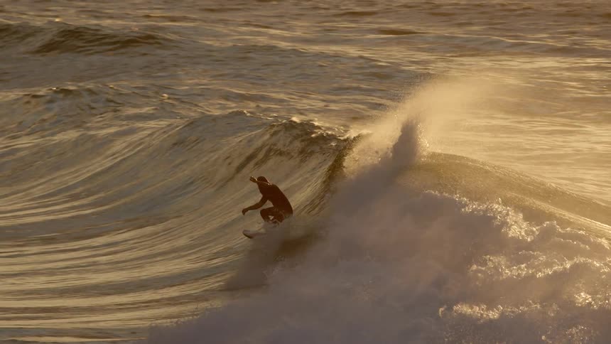 Surfer riding huge splashing wave that covers him as the sun reflects on the water