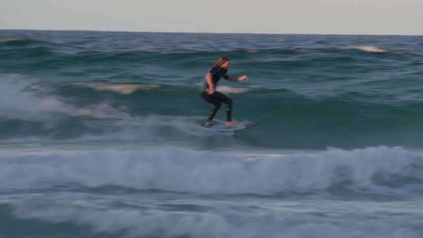 A surfer surfs at high speed across ocean waves during the day