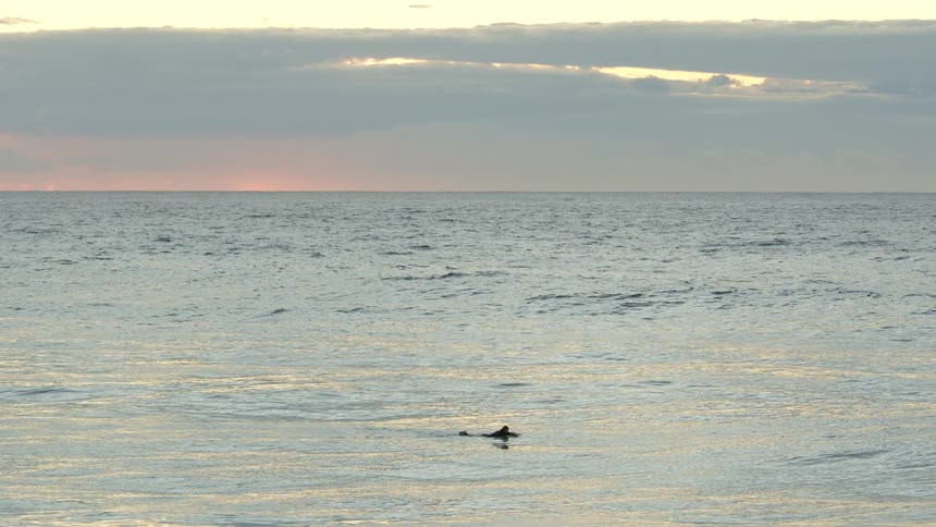 A person laying on a surfboard in the ocean with the sky and clouds in the background