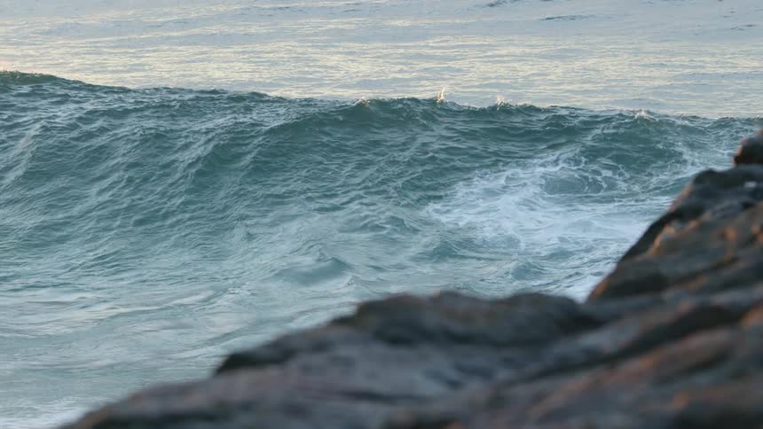 Big wave rolling in splashing near a rocky cliff