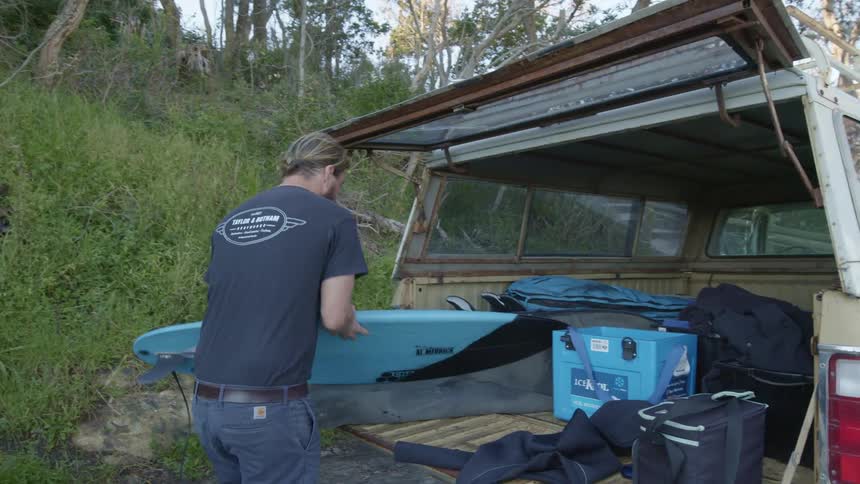 Bearded man removes a body board from a bag in the back of his pickup truck