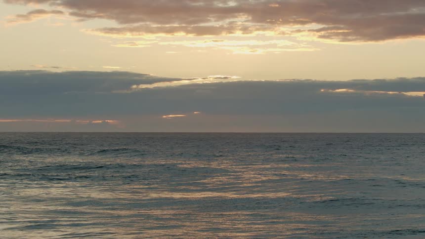 Wide shot of the horizon over the ocean at sunset with scattered clouds in the sky