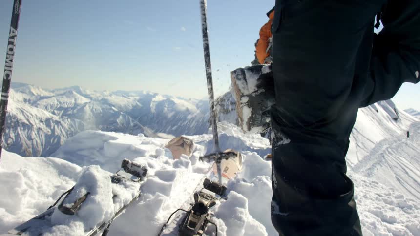 A person is cleaning off their ski poles while standing next to a pair of skis in the snow