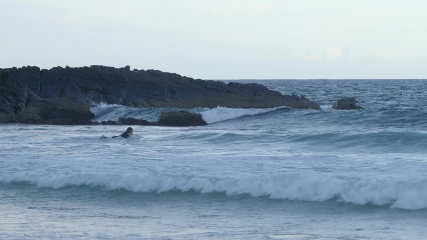 A man on his surfboard paddles in to the ocean