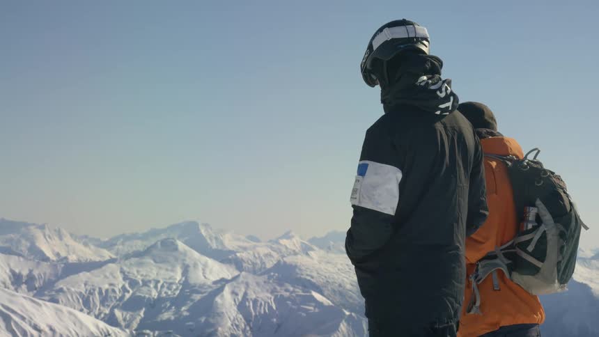 Two people stand overlooking view of snow covered mountain range