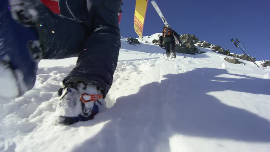 Two skiers steadily march up the side of a snow covered mountain