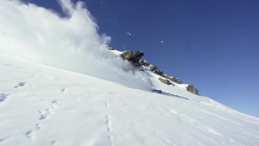 A person with a coat and backpack skiing down a snowy mountain with the sky and clouds in the background