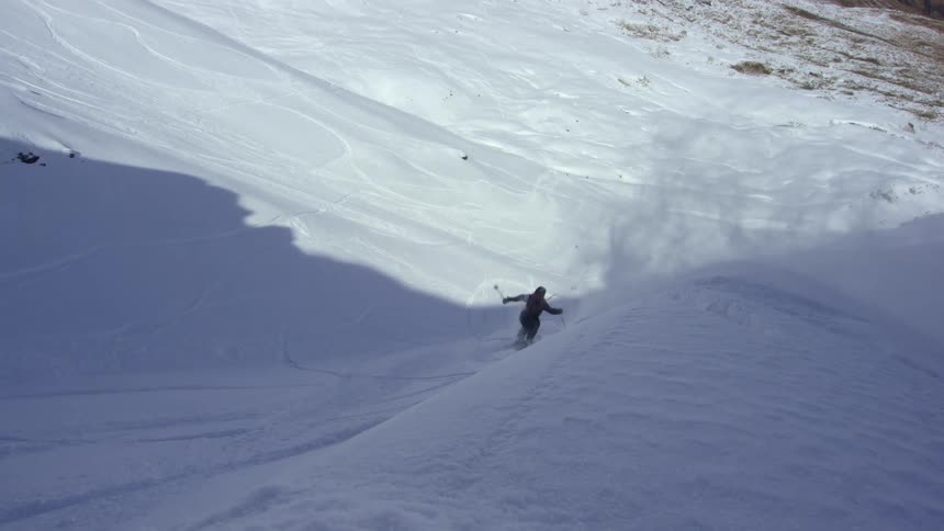 A skier turns and flips off a ledge down the snowy slope