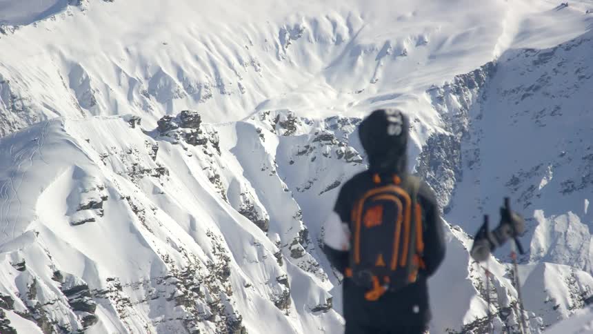 A person is wearing warm clothing and looking at snow covered mountains