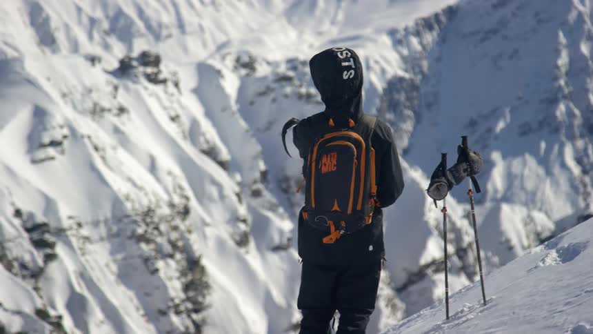 A person with a backpack and a coat standing on a snowy slope with a mountain in the background