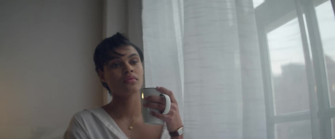 A woman holds a mug in her hand as she stands near a window
