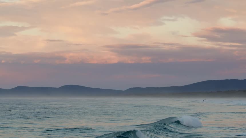 Small waves in the ocean next to the coast at sunset