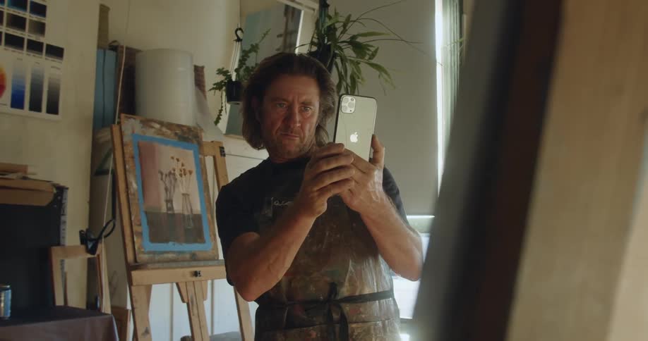 A male painter takes a photo of his art on an easel with his cell phone
