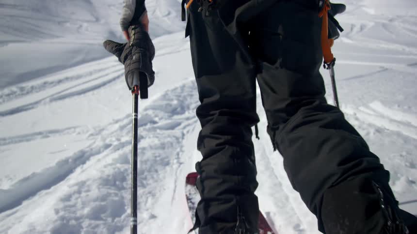 Man walks up snow covered slope wearing skis under clear sky